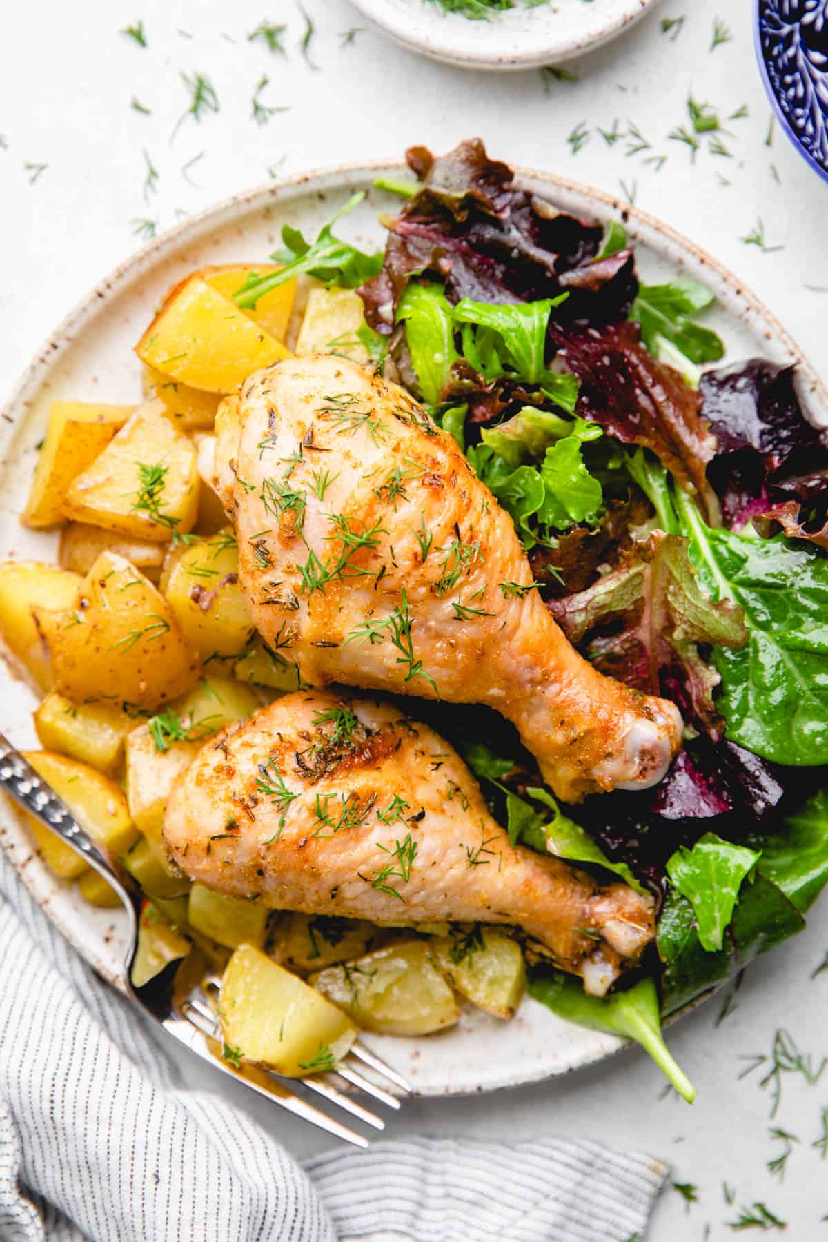 Chicken drumsticks with potatoes and salad on a plate.