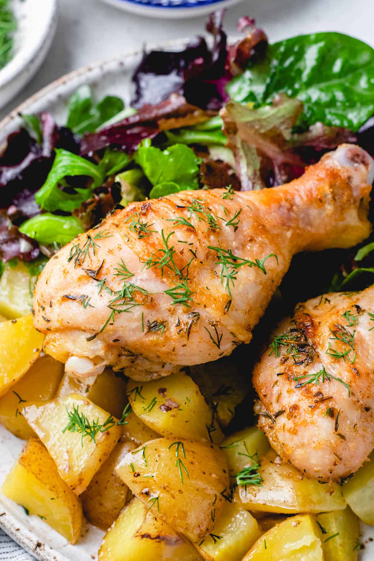 Chicken drumsticks with potatoes and salad on a plate.