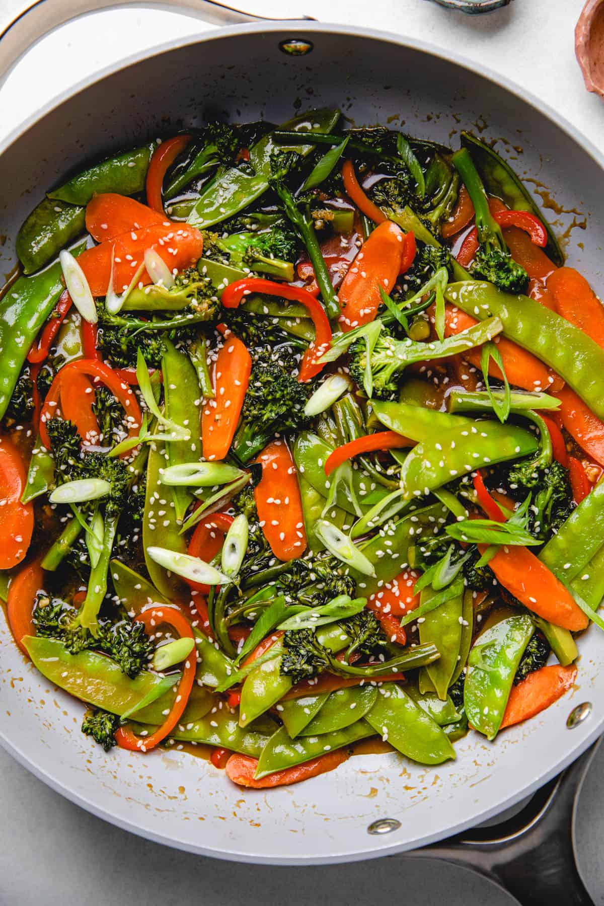 Sauteed broccoli, carrots, snow peas, and red bell pepper in teriyaki sauce in a skillet.