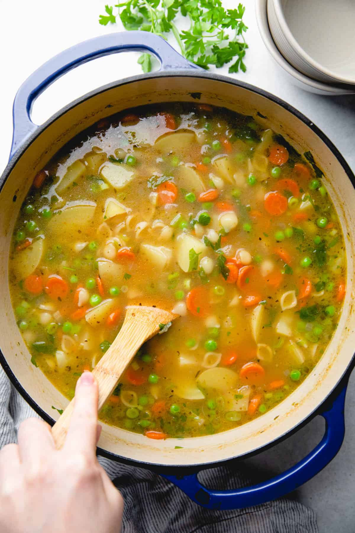 Soup with onions, carrots, potatoes, peas, and pasta in a pot.