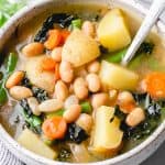 Soup with white beans, potatoes carrots, kale, and green beans in a bowl.