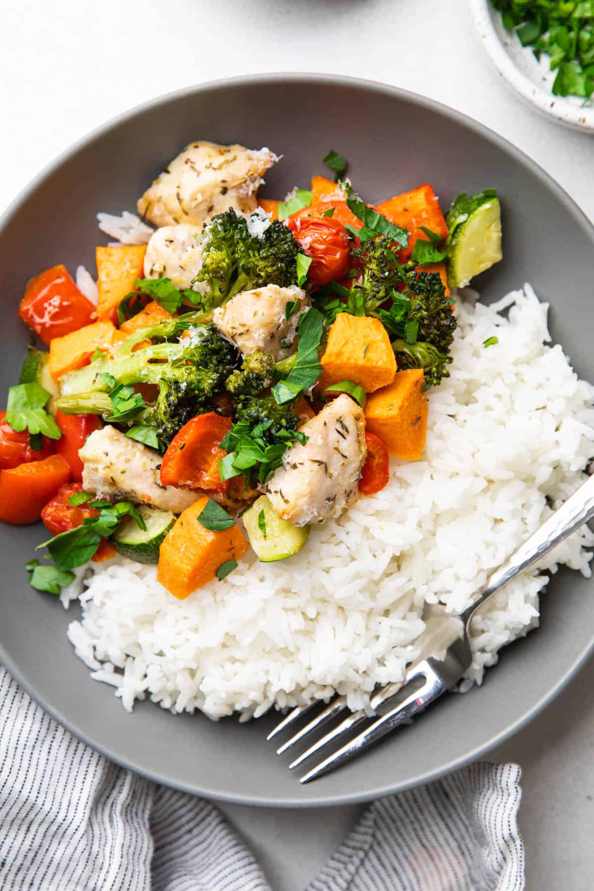 Baked diced chicken breast, sweet potatoes, broccoli, zucchini, bell pepper, and cherry tomatoes with white rice in a bowl.