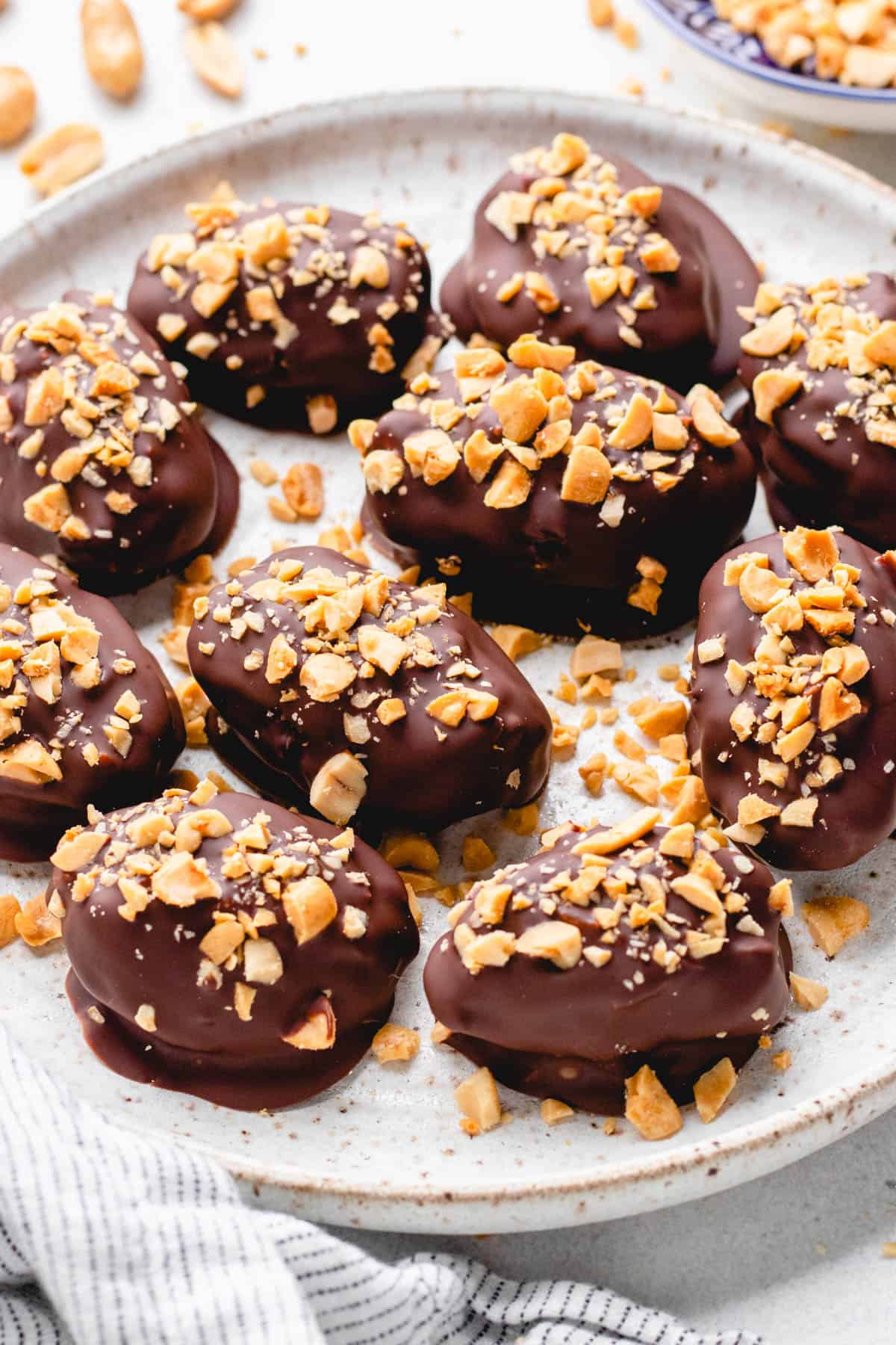 Dates, filled with peanut butter, covered with chocolate, and topped with chopped peanuts, on a white plate.