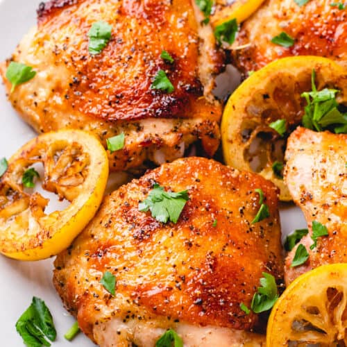 Bone-in Skin-on chicken thighs with seared lemon slices on a plate.
