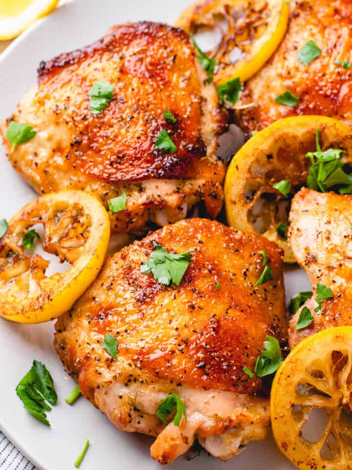 Bone-in Skin-on chicken thighs with seared lemon slices on a plate.