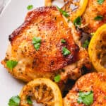 Bone-in Skin-on chicken thighs with seared lemon slices on a plate.