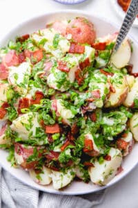 Red potato salad with dill and chopped bacon in a bowl.