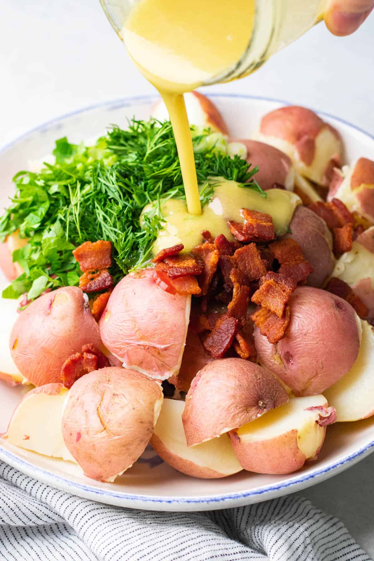 Pouring salad vinaigrette over red potatoes, cooked bacon and herbs.