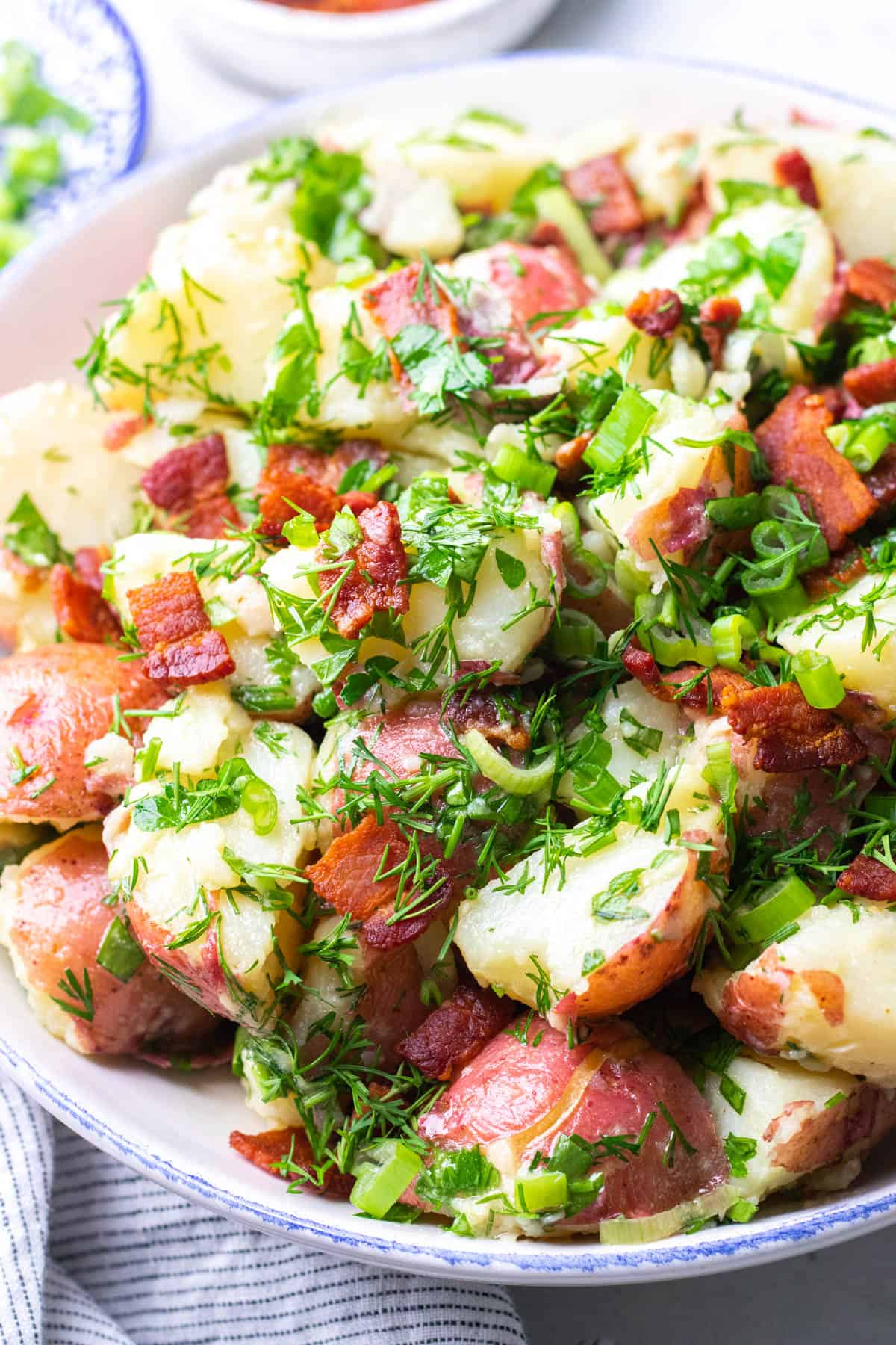 Red potato salad with dill and chopped bacon in a bowl.