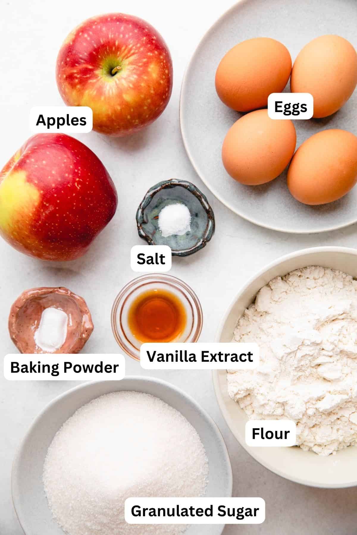 Apples, eggs, flour, sugar, vanilla extract, and salt in separate bowls.