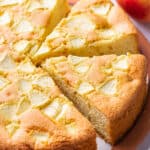 A sliced cake, topped with apples, sitting on a plate on a table.