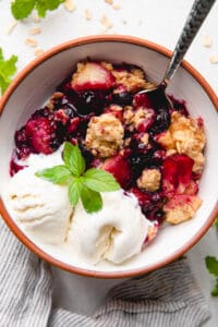 Apple and Blueberry Crumble with a spoon of ice cream and mint leaves in a bowl.