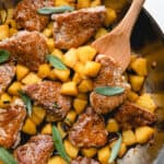 Pork medallions with caramelized apples in a skillet, topped with fresh sage leaves.