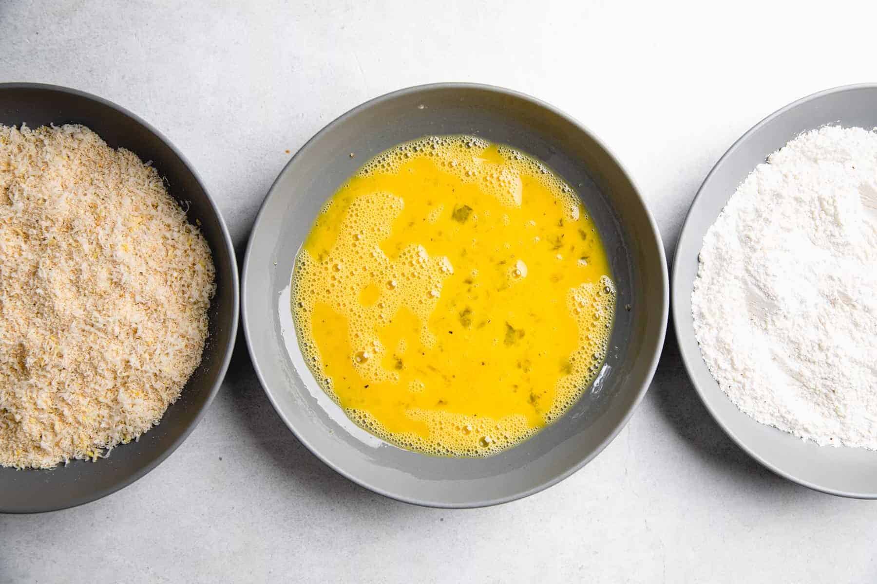 3 separate bowls, filled with flour, whisked eggs, and panko breadcrumbs.