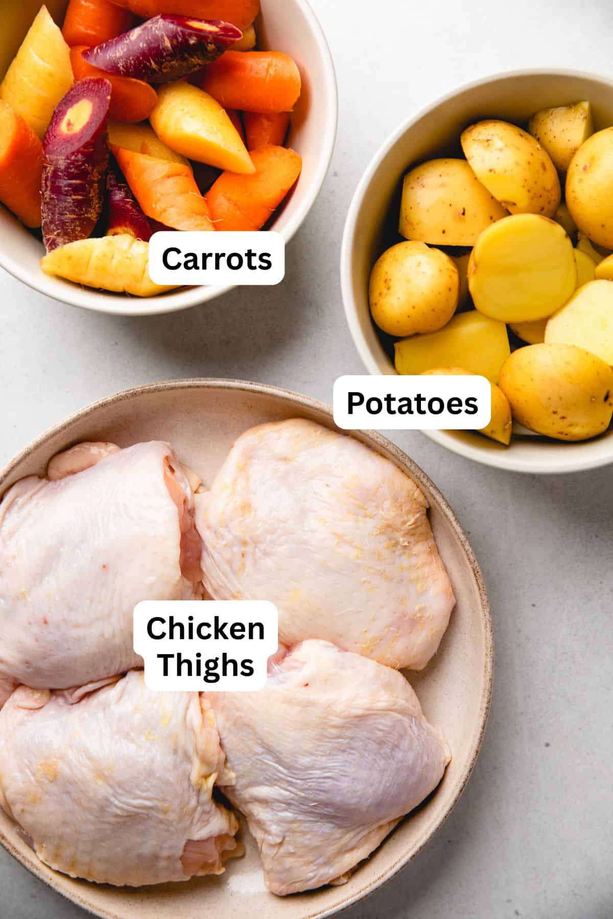 Chopped carrots, baby potatoes, and chicken thighs in separate bowls.