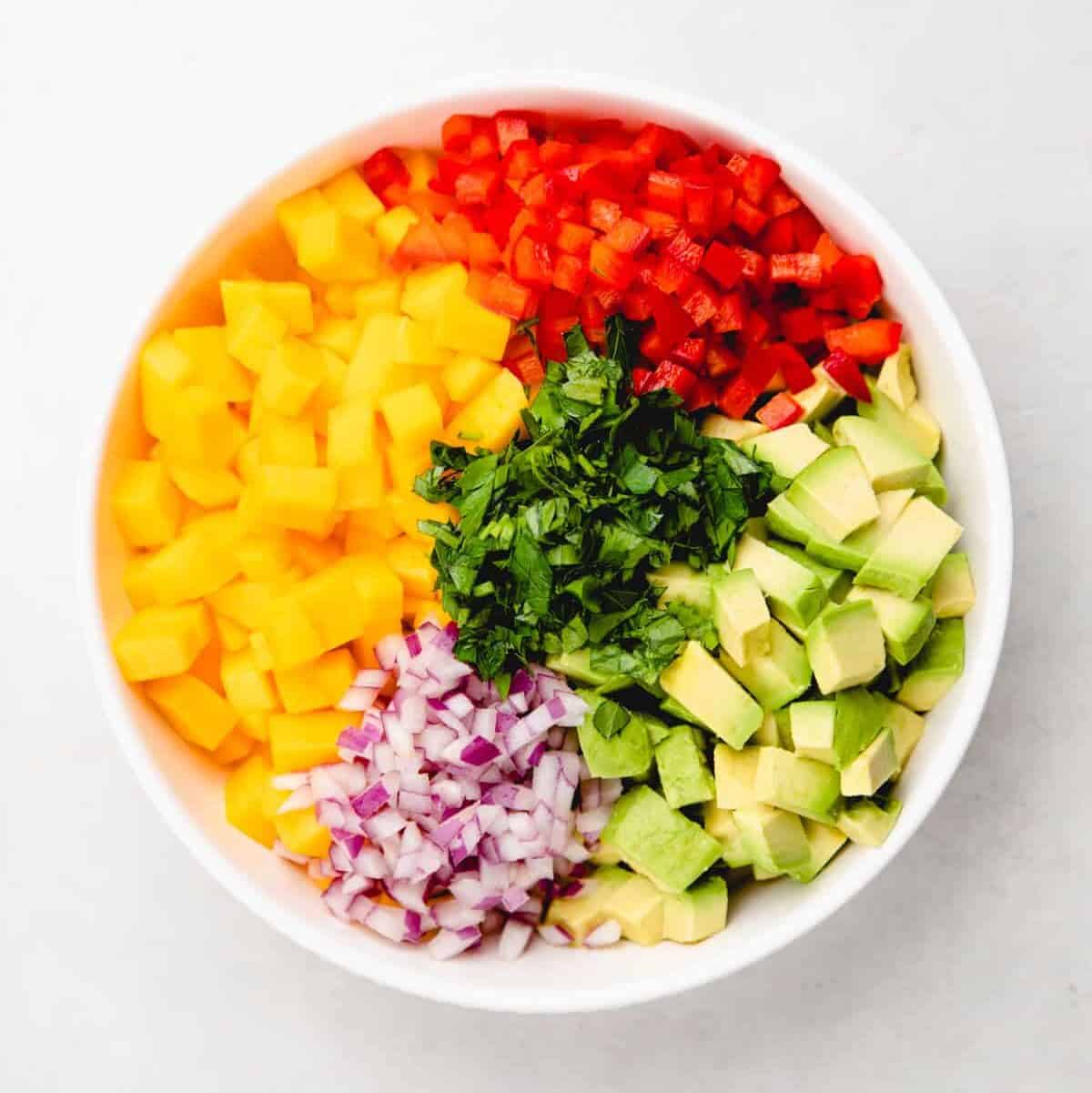 Chopped mango, bell pepper, avocado. red onion, and cilantro in a bowl.