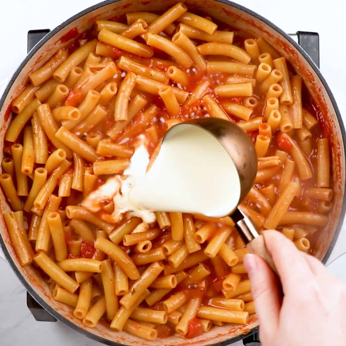 Adding heavy cream to baked ziti.