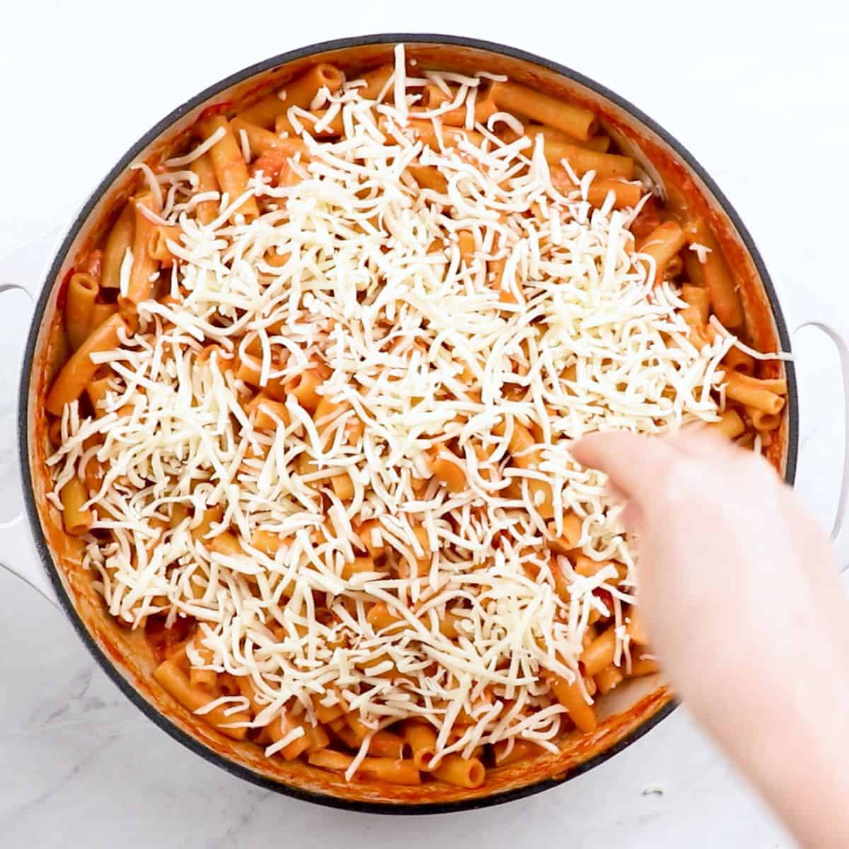Adding grated mozzarella cheese to baked ziti.